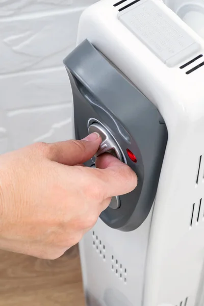Woman hand turning the thermostat knob of a home oil heater.