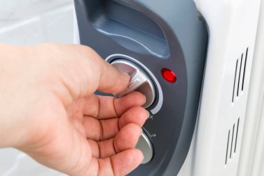 Kadın eli elektrikli yağ ısıtıcısının termostat düğmesini açıyor.