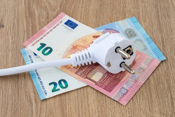 White power plug on euro banknotes over a brown wooden surface.