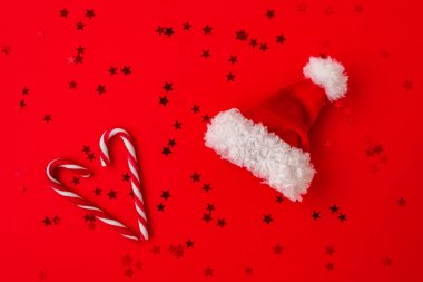 Santa Claus red hat and two candy canes on a red background.