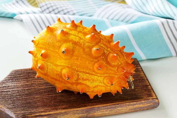 Kiwano laranja fresco inteiro em uma placa de corte de madeira marrom — Fotografia de Stock