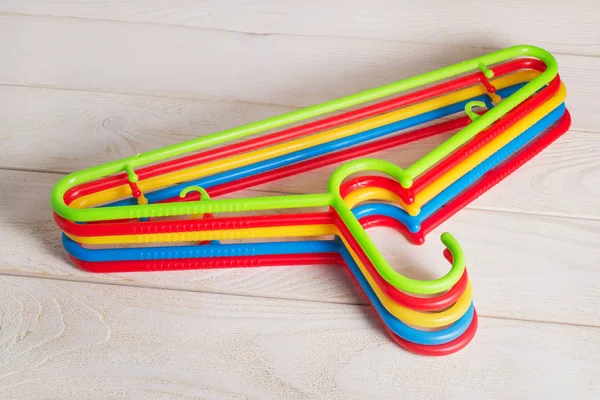 Five multicolored plastic clothes hangers on a wooden surface.