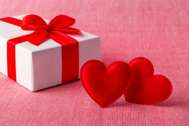 Kırmızı kurdeleli beyaz hediye kutusu ve iki tane ipek sevgililer günü kartı.