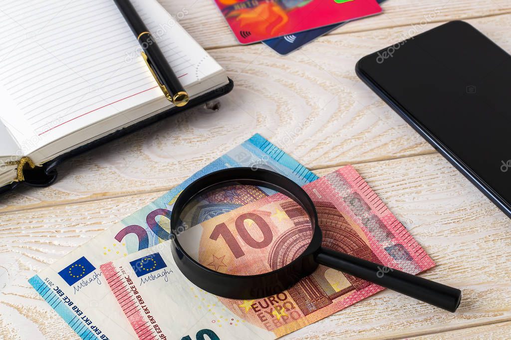 Magnifier on euro banknotes near pen, note book, credit cards