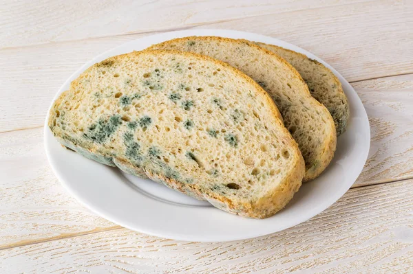 Кусочки черствого хлеба с зеленой плесенью на белой тарелке — стоковое фото
