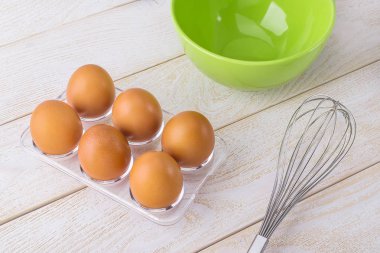 Şeffaf plastik tepside tavuk yumurtası, yeşil kase ve çırpı.