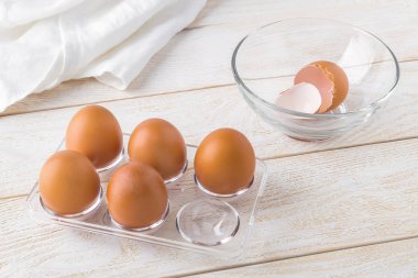 Şeffaf plastik tepside beş çiğ tavuk yumurtası ve yumurta kabuğu.