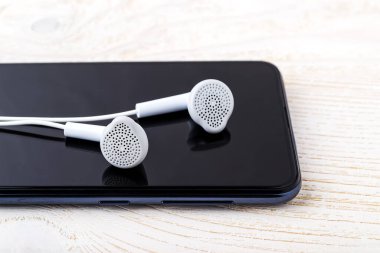 Siyah bir akıllı telefon ekranında beyaz kulaklıkları yakın çekim. Müzik dinle. Müzik ve iletişim için dokunmatik ekranlı modern kişisel cihaz. Ön görünüm.