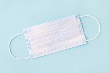 Mavi arka planda tek kullanımlık cerrahi maske. Üç katmanlı tıbbi maske bakterilerden, virüslerden ve tozdan korur, enfeksiyon riskini azaltır. Havadan bulaşan hastalıkları koruma kavramı.