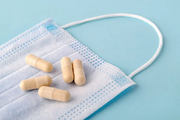 Pills or capsules on a disposable surgical mask over a blue background. Medical mask reduces the risk of infection. Airborne disease protection concept. Close-up.