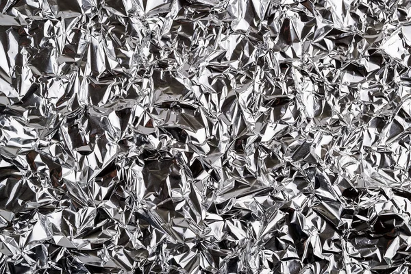 Crumpled aluminum foil texture. Sheet of creased silver foil with shiny folds for background. Metal wrinkled surface as graphic resource. Top view.