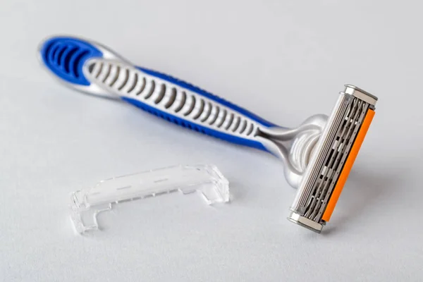 New disposable shaving razor with triple blade on a pastel gray background. Silver blue plastic razor with orange lubricat strip. Personal hygiene accessory for man and woman.