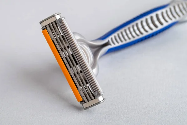 Close-up of new disposable shaving razor with triple blade on a pastel gray background. Silver blue plastic razor with orange lubricat strip. Personal hygiene accessory for man and woman.