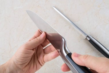 Kadın elleri bileme çeliğini kullandıktan sonra profesyonel şef bıçağını kontrol ediyor. Yüksek karbonlu molibdenum vanadyum çelikten yapılmış modern mutfak aletleri. Üst görünüm. 