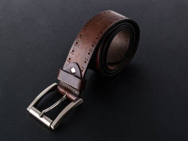 Siyah bir yüzeyde klasik metal tokalı hakiki deriden yapılmış kahverengi kuşak. Erkeklerin şık deri aksesuarları. Gösterişsiz görüntü. Ön görünüm.