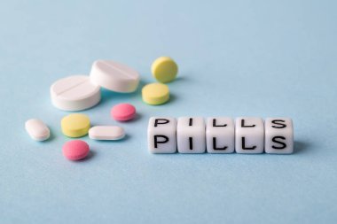 Beyaz küplerden yapılmış kelime hapları ve mavi tıbbi arka planda farklı haplar. Hastalanmak, hap almak ya da tedavi olmak için. Sağlık hizmetleri. Ön görünüm.