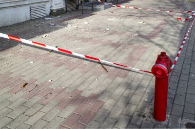 Kırmızı beyaz sinyal bandı, eski bir binanın tamiri sırasında kaldırımın bir kısmını inşaat enkazıyla kaplıyor. Şehir caddesinde düşen nesnelere dikkat et.. 