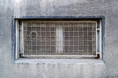 Dikdörtgen bodrum ya da bodrum penceresi tel metal ağ ve ızgarayla sıkılaştırılmış. Eski gri bir binanın duvarındaki teknik kat penceresi. Ön görünüm.