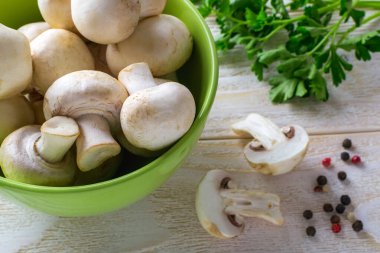 Tahta bir masada maydanozun yanında yeşil bir kasede taze taze şampiyonlar. Sebze proteini olarak mantar, çiğ gıda diyeti, vejetaryenlik. Üst görünüm.