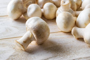Beyaz ahşap bir masada taze taze taze şampiyonların yakın çekimi. Sebze proteini olarak mantar, çiğ gıda diyeti, vejetaryenlik. Ön görünüm.