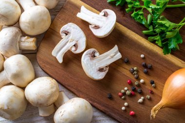 Tahta bir kesme tahtasının üzerinde üç parça şampiyon, biber, soğan ve maydanoz. Sebze proteini olarak mantar, çiğ gıda diyeti, vejetaryenlik. Üst görünüm.