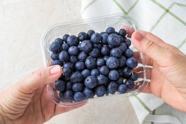 Kadın eli, şeffaf bir yiyecek kabını olgun, tatlı yaban mersiniyle tutuyor. Meyve ve böğürtlen, vejetaryen ve sağlıklı beslenme. Süper yemek. Yemek hazır. Üst görünüm.