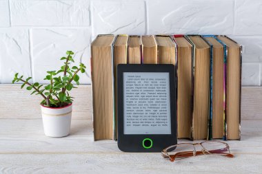 E-okuyucu, kağıt kitapların yanında saksı bitkisi ve görüş gözlükleri beyaz ahşap bir masada. Boşluğu e-kitap ekranına kopyala. Zevk ve eğitim için e-okuma. Ön görünüm.