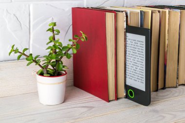 Kağıt kitaplar ve küçük saksı bitkileriyle dolu bir rafta e-okuyucu. Boşluğu e-kitap ekranına kopyala. Zevk ve eğitim için e-okuma. Ön görünüm.