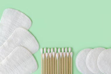 Tek kullanımlık iç çamaşırları, pamuk pedleri ve pamuk tomurcukları, naneli pastel bir arka planda. Kadınsı hijyen malzemelerinin olduğu düz bir yatak. Uzayı kopyala Üst görünüm.