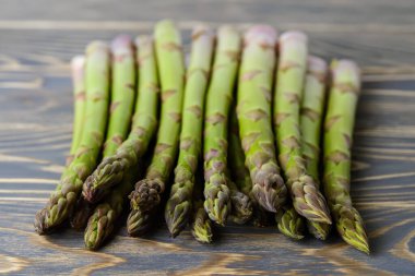 Koyu yeşil bir ahşap masada taze taze kuşkonmaz sapları. Sağlıklı beslenme, vejetaryen ve çiğ gıda diyeti için. Ön görünüm.