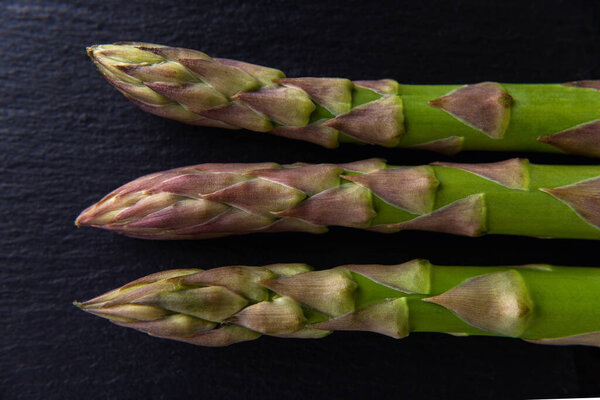 Top view of three fresh raw green asparagus stalks on a black background. Ingredient for healhy eating, vegetarian and raw food diet. Close-up. 