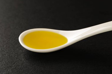 Beyaz bir Çin porselen kaşığının içinde siyah bir taş servis tahtasının üzerinde zeytin yağı. Et, balık ve sebze için sos ve baharatlar. Ön görünüm.