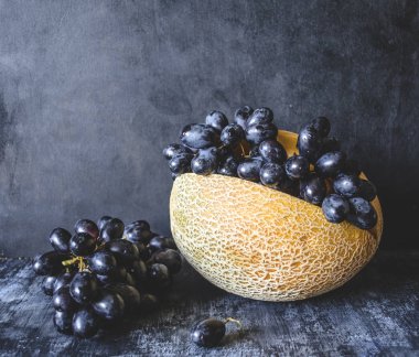 Turuncu kavun ve karanlık bir arka plan üzerinde siyah üzüm. Natürmort.