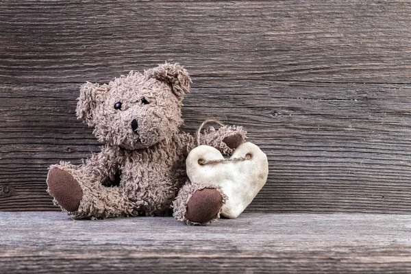 Urso de pelúcia com coração sentado no fundo de madeira velha . — Fotografia de Stock