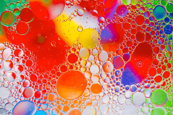 Gotas de aceite en el agua sobre un fondo coloreado — Foto de Stock