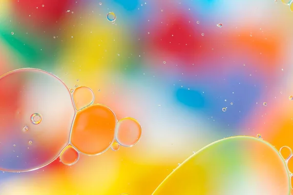 Gotas de aceite en el agua sobre un fondo coloreado —  Fotos de Stock