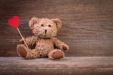 Oyuncak ayı ile eski ahşap arka plan üzerinde oturan kalp.