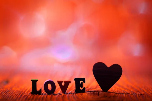 Надпись любовь и деревянное сердце на размытом фоне — стоковое фото