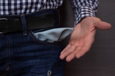 Kot pantolonlu, cebi boş bir iş adamı. Koyu gri arka planda işsiz, meteliksiz, iflas, kötü kredi, borç ve finansal konsept için boş kot cepleri gösteren genç adam