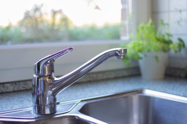 Yan manzara temiz krom mutfak lavabosu ve arka planda güzel bahçe manzaralı bir pencere. Güzel ve modern mutfak kavramı. Mermer tezgah