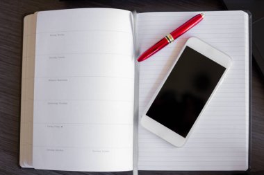 Kağıt defterin üst görüntüsünü kırmızı kalemle kapat. Siyah ekranlı akıllı telefon ve metin için alanı kopyala