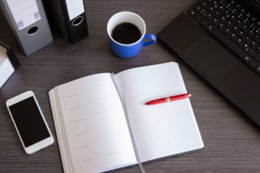 Laptop, akıllı telefon, malzeme ve bir fincan kahveyle birlikte koyu renkli bir ofis masası. Kopyalama alanı olan üst görünüm