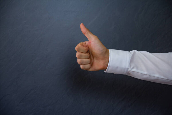 Young successful Businessman showing thumbs up. light anthracite Background with copy space for text. Cropped close up shot of a hand