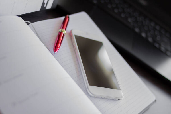 Close up of a paper notebook with a red pen. Smart phone with a black screen and copy space for text