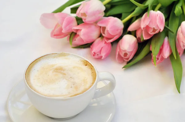 cup of coffee and bouquet of tulips on white background