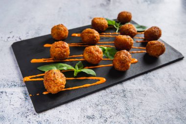 Fried potato cheese balls or croquettes with orange sauce and green salad. Selective focus