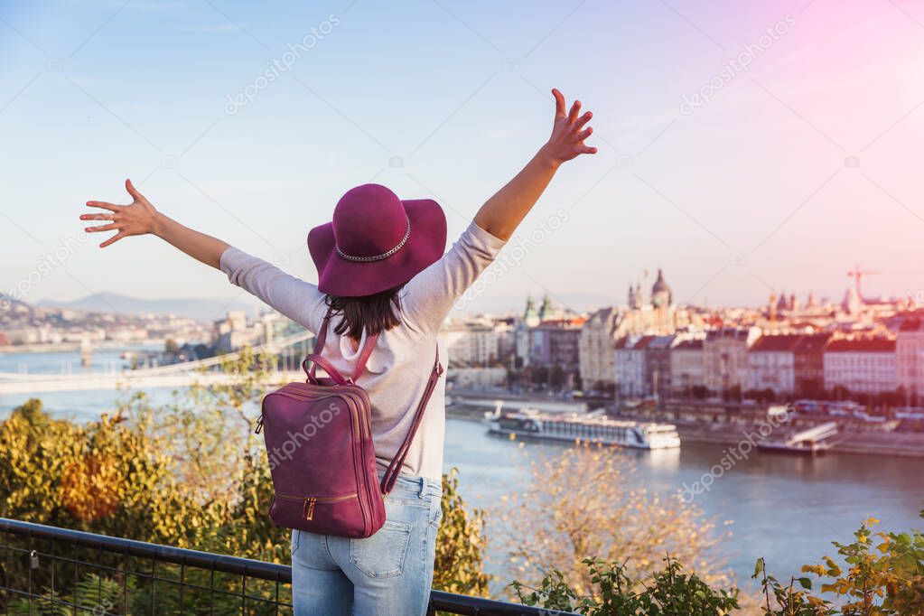 A happy young woman enjoying her trip to Budapest, Hungary from the point from Gellert Hill during sunrise in autumn during sunrise.