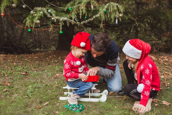 Отец и две дочери открывают подарки боксы возле елки на открытом воздухе во дворе дома . — стоковое фото