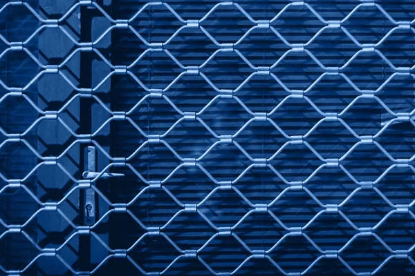 Textura de ferro de uma grelha de aço em persianas vermelhas na porta. Fundo azul . — Fotografia de Stock