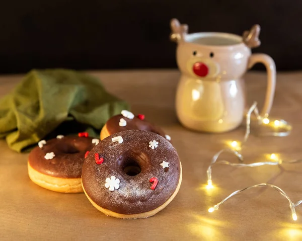 Mesa de desayuno de Navidad con rosquillas de chocolate decoradas con espolvoreos rojos y blancos con cacao caliente en taza de ciervo — Foto de Stock